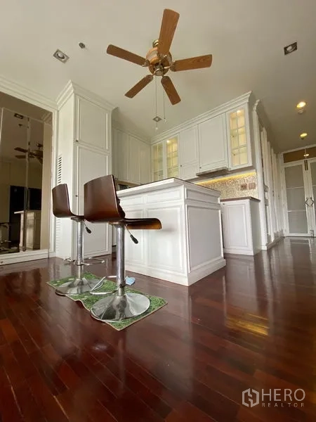 Condominium for rent in Ratchathewi, Bangkok - White kitchen with island breakfast bar, ceiling fan, and hardwood flooring.