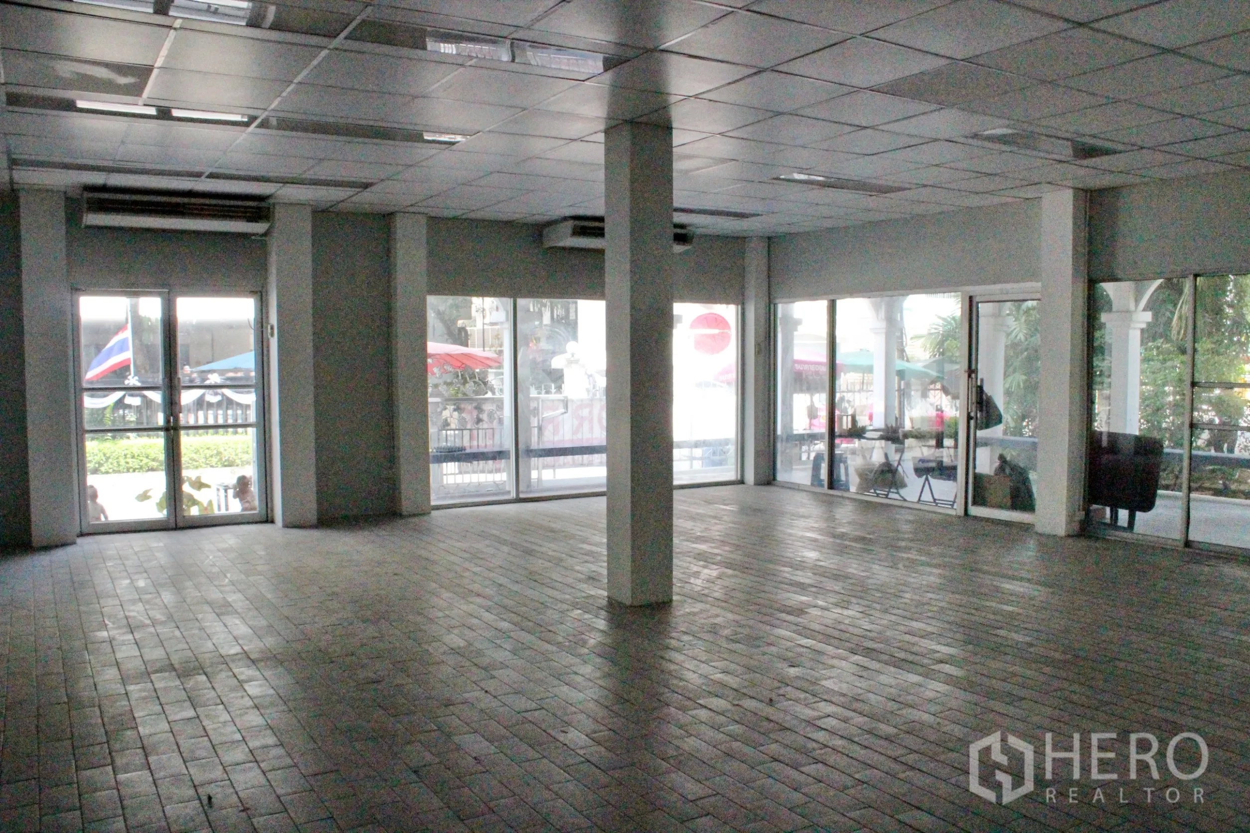 Home Office for rent in Khlong Toei, Bangkok - Large open-plan office hall with tiled floor, grid ceiling, columns and expansive glass doors and windows.