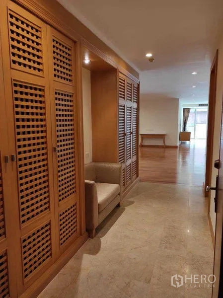 Condominium for rent in Khlong Toei, Bangkok - Hallway with built‑in lattice wood closets and a small seating nook opening to the living area.