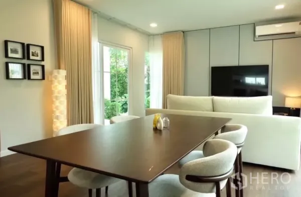 独立式住宅 出租在Bang Phli, Samut Prakan - 开放式客餐厅，木地板，大窗与米色窗帘，墙挂电视。