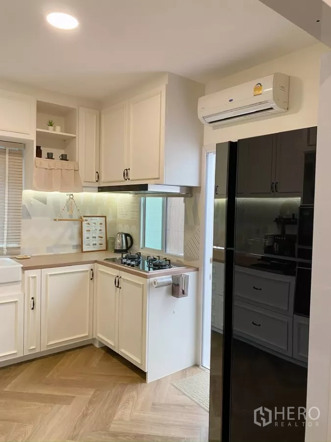 Detached House for sale in Sai Mai, Bangkok - Compact kitchen with white cabinetry, gas cooktop and black refrigerator.