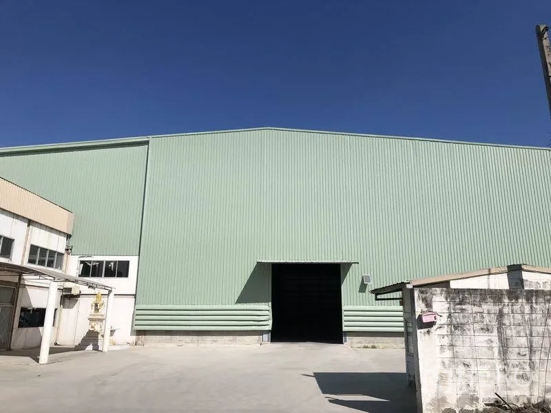 Factory for rent in Bang Phli, Samut Prakan - Front facade of green warehouse with a wide loading door opening to a paved yard.