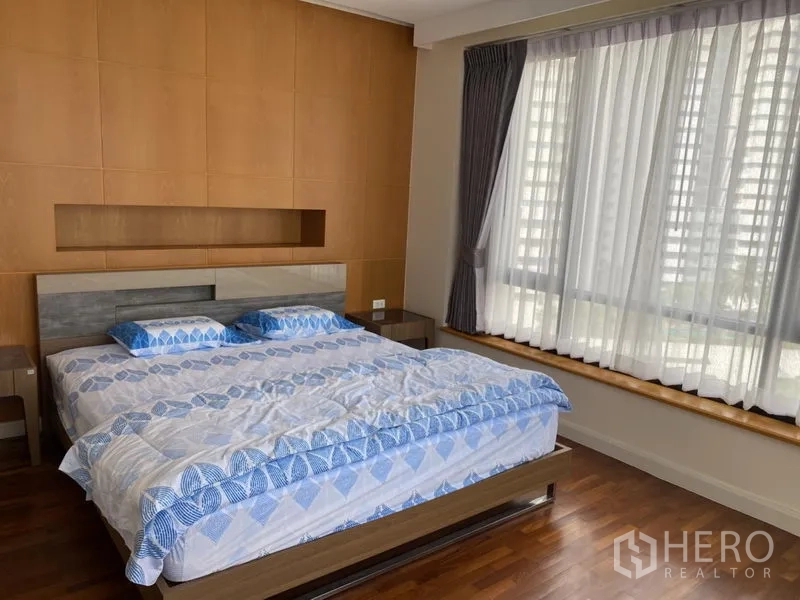 Condominium for rent or sale in Sathon, Bangkok - Primary bedroom with king bed, large bay window and a wood-paneled feature wall.