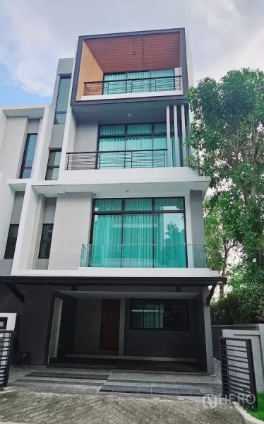 Townhouse for rent in Saphan Sung, Bangkok - Modern 4-storey corner townhouse facade with balconies, glass railings and covered parking.