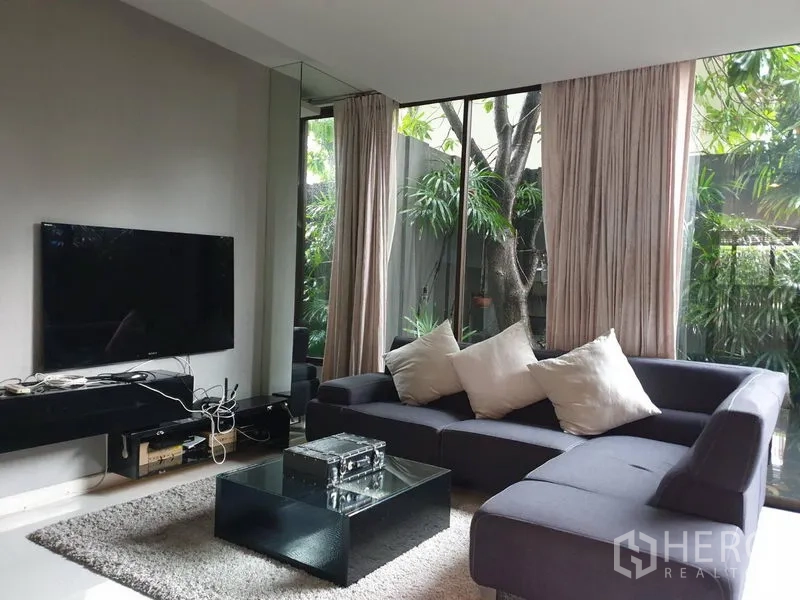 独立式住宅 出售在Watthana, Bangkok - 现代客厅，转角沙发、电视墙，落地窗望向花园。