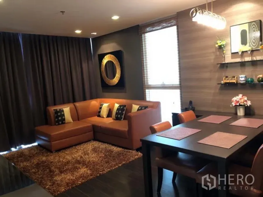 公寓 出租或出售在Watthana, Bangkok - 曼谷公寓客餐厅一体空间，暖色L形皮沙发、深色窗帘、壁架与吊灯