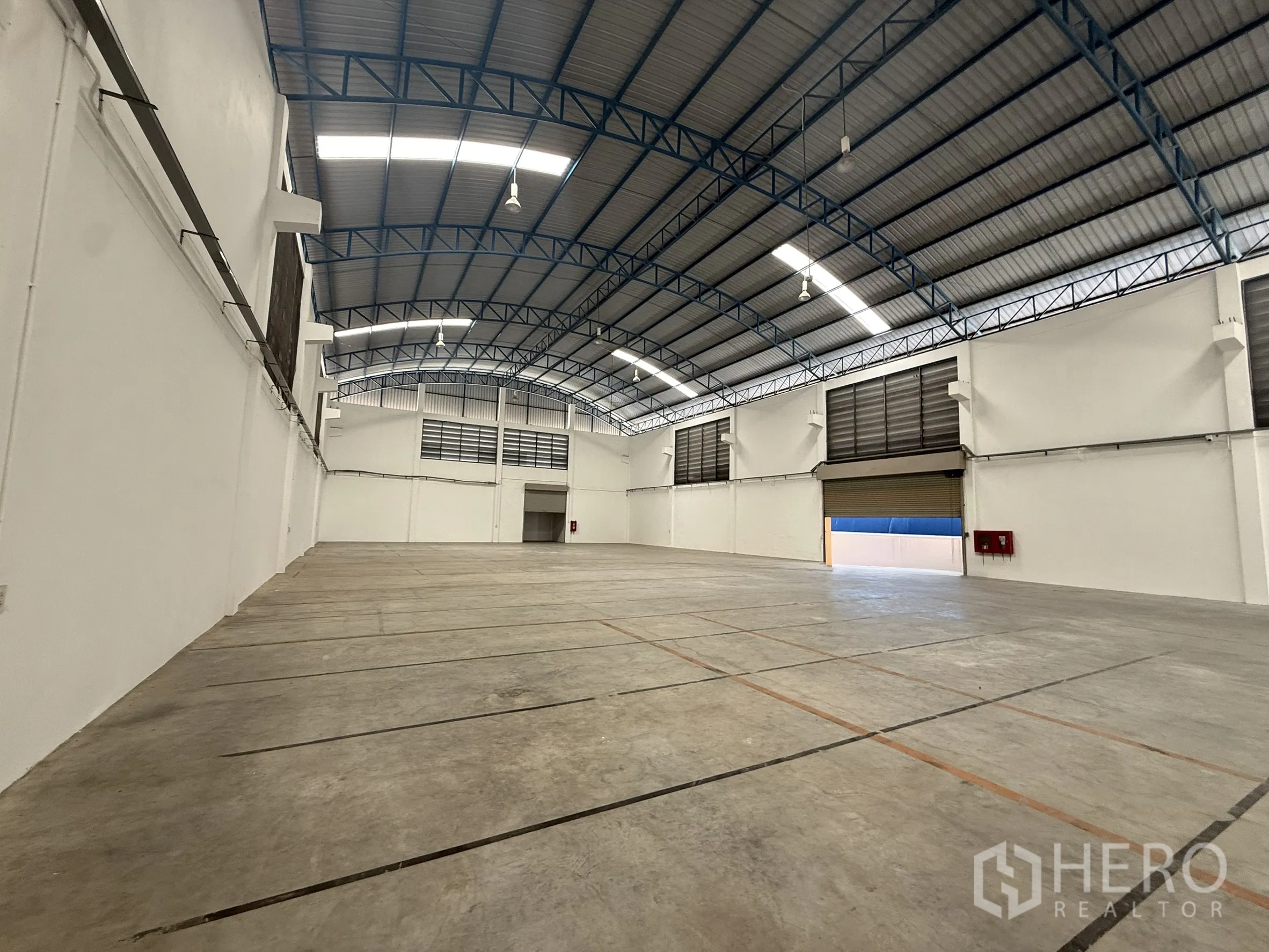 Warehouse for rent or sale in Bang Bo, Samut Prakan - Large warehouse bay showing roller shutters, louvered vents and wall‑mounted fire hose cabinet.