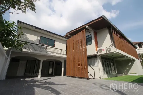 独立式住宅 出租在Chatuchak, Bangkok - 院落视角的两层住宅，铺砖露台，小片草坪与竖向木格栅，在蓝天下。