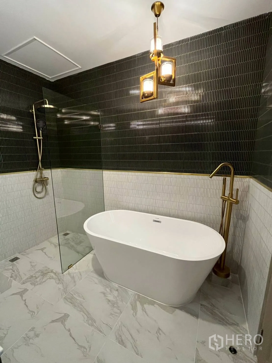 联排别墅 for rent in Khlong Toei, Bangkok - 浴室一角展示浴缸、金色龙头、玻璃隔断与吊灯。