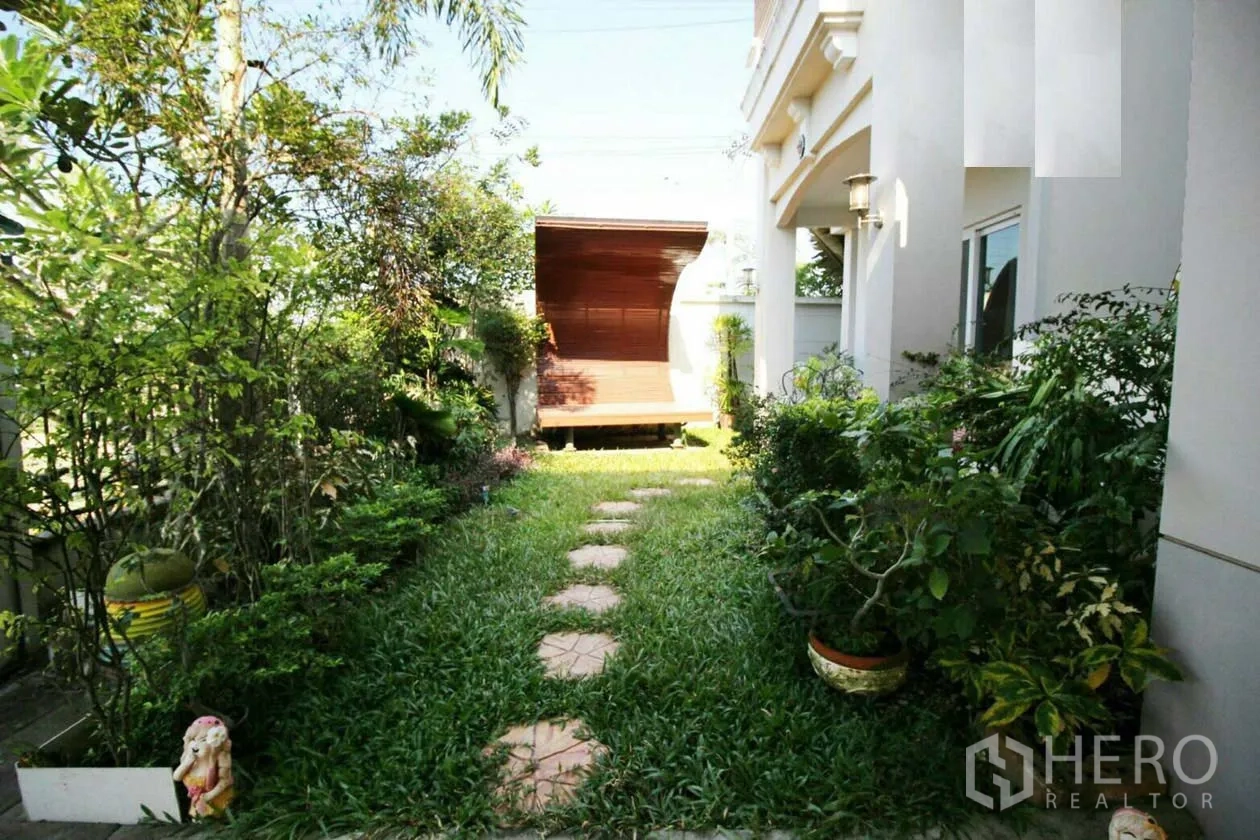 Detached House for rent or sale in Lat Krabang, Bangkok - Green side garden with stepping-stone path, dense plants and a small wooden pavilion.