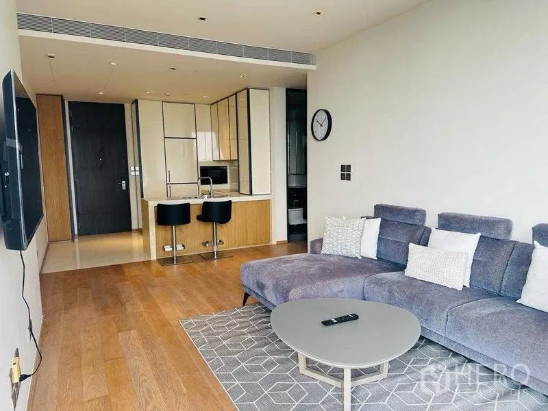 Condominium for rent in Khlong Toei, Bangkok - Living room facing a compact kitchen and entrance with wood flooring throughout.