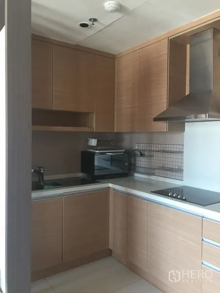 Condominium for rent - Compact U-shaped kitchen with wood cabinets, electric hob, and stainless range hood.