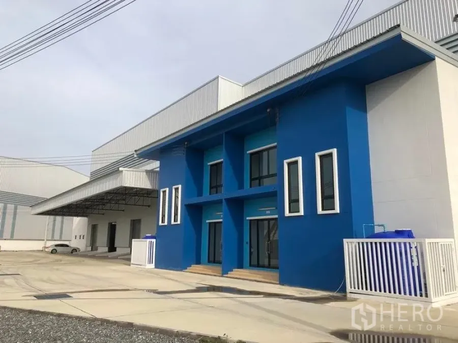 Factory for rent in Samut Prakan - Bang Sao Thong factory exterior with bright blue two‑storey office, wide driveway and covered loading bay in Samut Prakan.