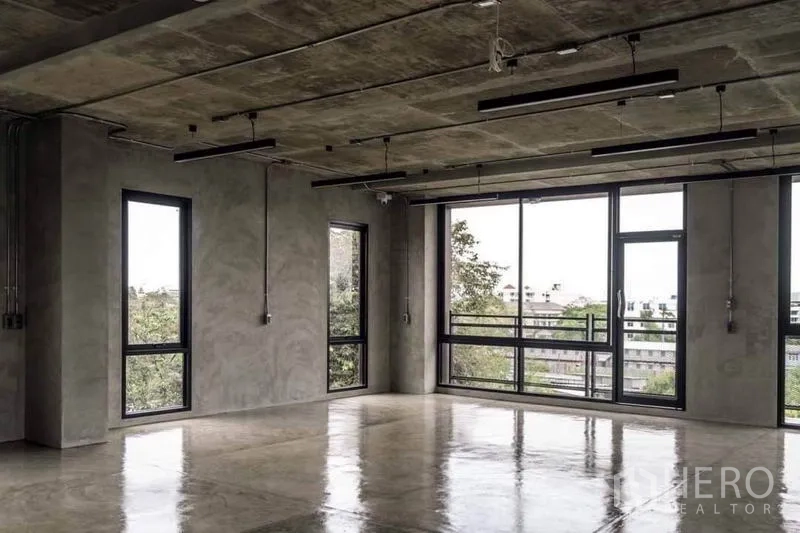 Home Office for rent or sale in Lak Si, Bangkok - Spacious workspace with floor-to-ceiling windows, balcony door and concrete finishes.