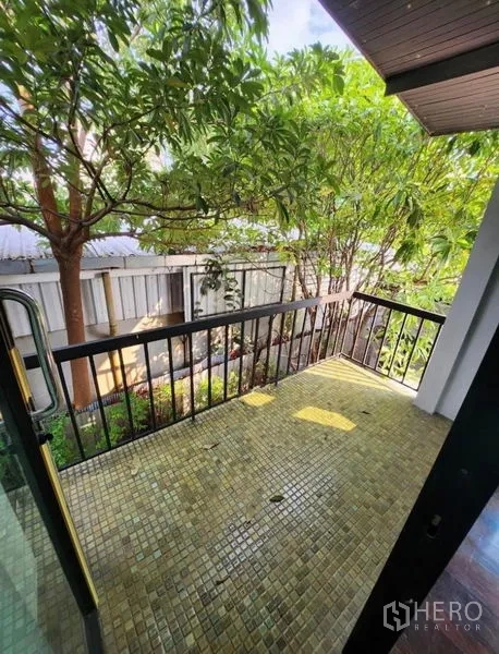 Home Office for rent in Lat Phrao, Bangkok - Small tiled balcony with black railing facing leafy trees and garden views.
