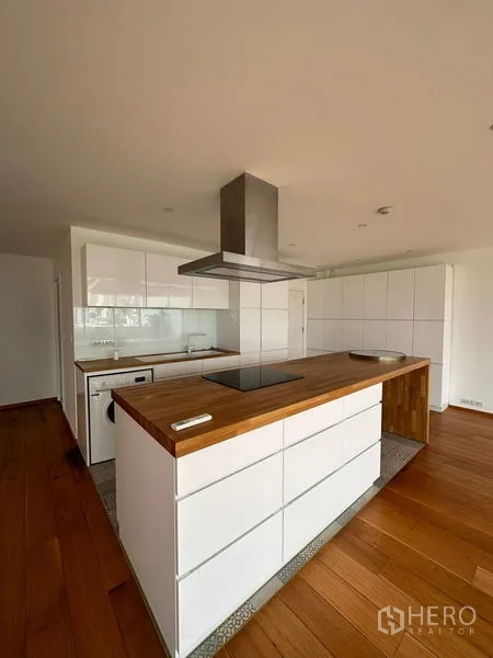 Condominium for rent in Khlong Toei, Bangkok - Close-up of sleek white kitchen island with wood countertop and stainless range hood.