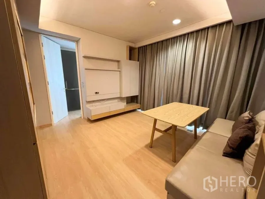 Condominium for rent or sale - Cozy living area with sofa and coffee table opening to hallway and curtained window.