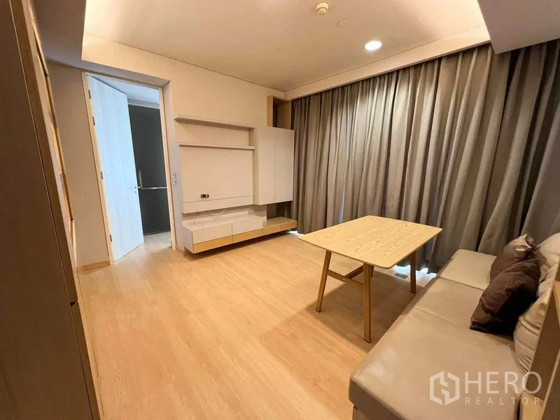 Condominium for rent or sale - Cozy living area with sofa and coffee table opening to hallway and curtained window.