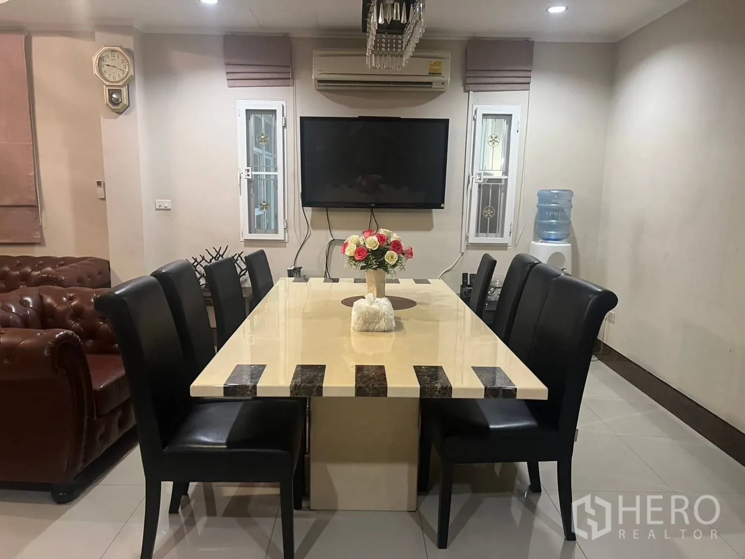 บ้านเดี่ยว for rent in Pak Kret, Nonthaburi - ห้องทานอาหารโต๊ะท็อปหินยาว เก้าอี้สีดำแปดที่นั่ง ทีวีผนัง และตู้กดน้ำ