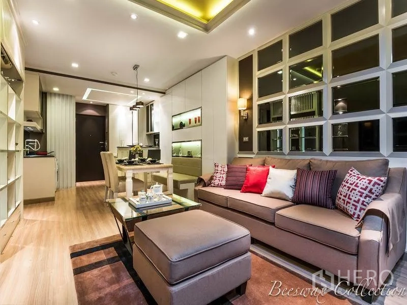Condominium for rent in Watthana, Bangkok - Contemporary living and dining area with sofa, ottoman, glass coffee table, built‑in shelving and an open kitchen under recessed lighting.