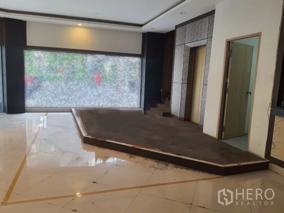 Shophouse for rent in Khlong Toei, Bangkok - Ground-floor retail area with large frosted display window, raised platform, elevator access and glossy tiled floor.