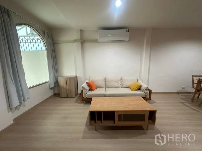 Townhouse for rent or sale in Phra Khanong, Bangkok - Cozy living corner with sofa, arched window and air-conditioning.