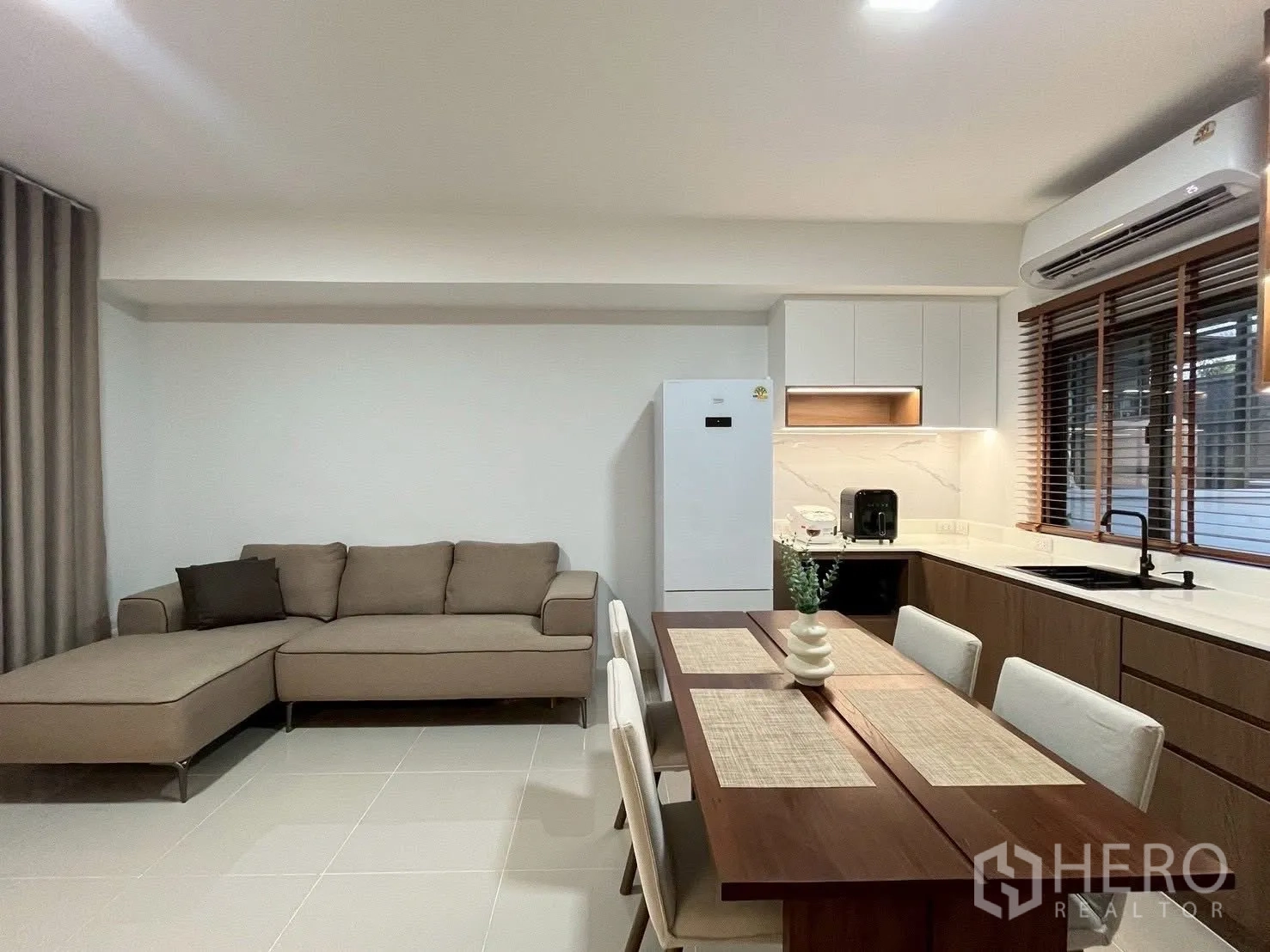 Townhouse for rent in Bang Phli, Samut Prakan - Living area with L-shaped sofa beside the dining table and fitted kitchen.