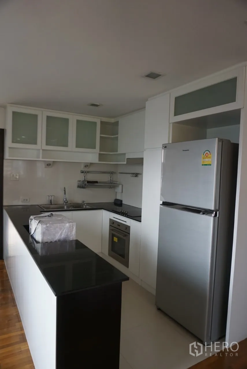 公寓 出租在Watthana, Bangkok - L形现代厨房，黑色石材台面、白色橱柜、不锈钢冰箱与烤箱