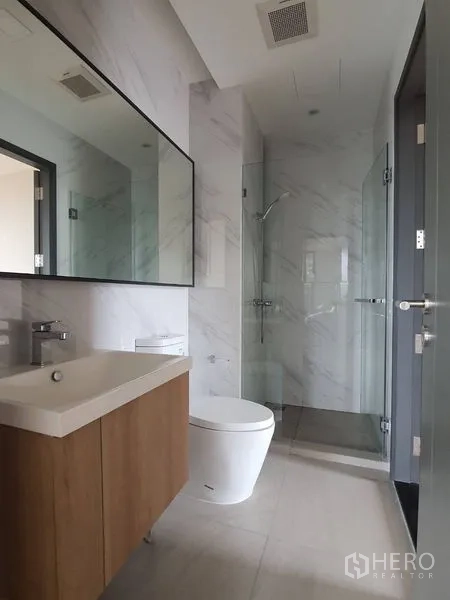 Condominium for sale in Huai Khwang, Bangkok - Guest bathroom with wall-mounted vanity, toilet and glass-enclosed shower.