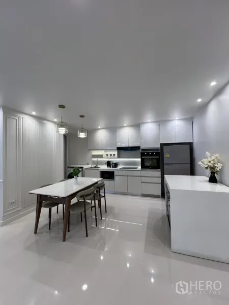 Condominium for rent in Yan Nawa, Bangkok - Sleek white kitchen with built-in oven, microwave, fridge, and a marble dining table under pendant lights.