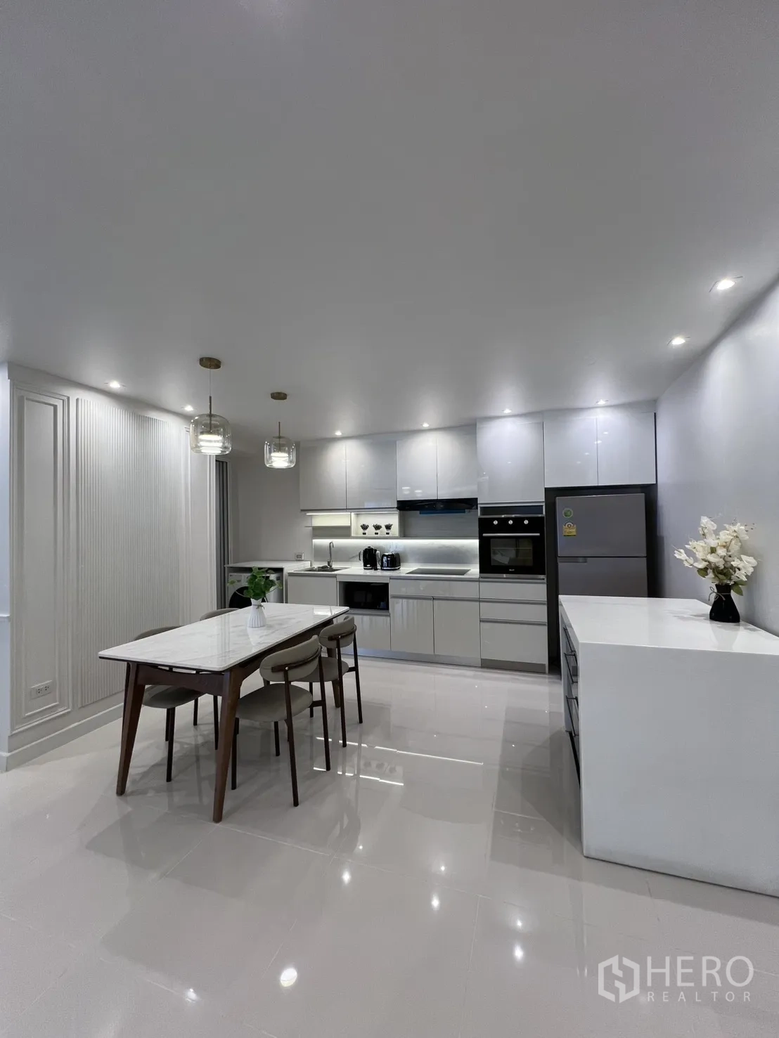 Condominium for rent in Yan Nawa, Bangkok - Sleek white kitchen with built-in oven, microwave, fridge, and a marble dining table under pendant lights.