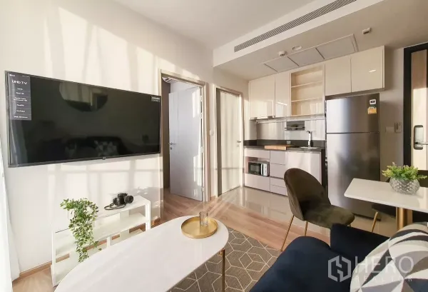 Condominium for rent in Khlong Toei, Bangkok - Living area facing kitchenette with large TV and dining nook.