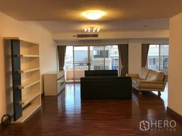 Condominium for rent in Sathon, Bangkok - Large living room with built-in shelving, leather sofas, and sliding doors to the balcony.