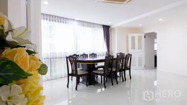 Condominium for rent or sale in Khlong Toei, Bangkok - Bright dining area with long wooden table, sheer curtains and glossy white floors.