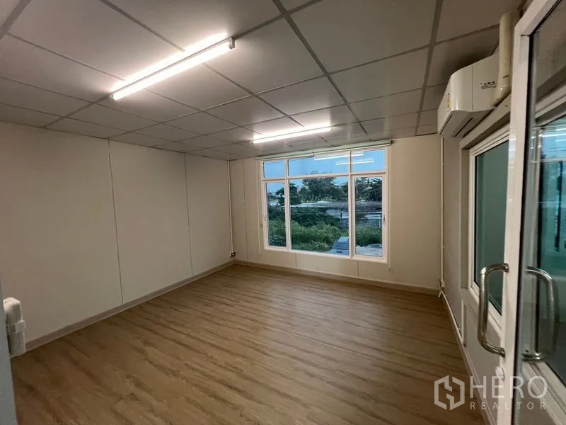 Warehouse for rent in Prawet, Bangkok - Spacious office with big windows overlooking greenery and an air-conditioning unit.