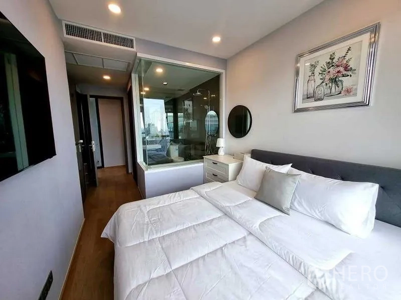 公寓 出租在Bang Rak, Bangkok - 卧室配玻璃隔断通向浴室，筒灯与木地板营造温馨感。