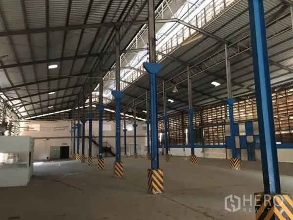 Warehouse for rent in Bang Kapi, Bangkok - Spacious warehouse interior with high steel roof, blue columns, and concrete floor in Bang Kapi.