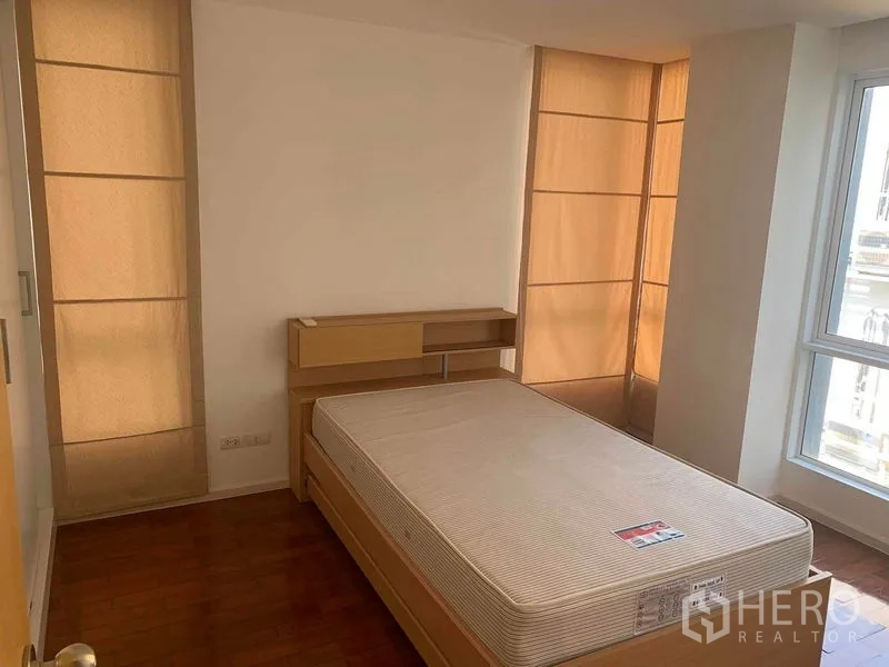 Condominium for rent or sale in Khlong Toei, Bangkok - Minimal bedroom with single mattress, built-in headboard, and tall windows.