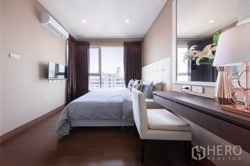 Condominium for rent in Watthana, Bangkok - Bedroom with large window, dressing table, upholstered headboard, and soft lighting.