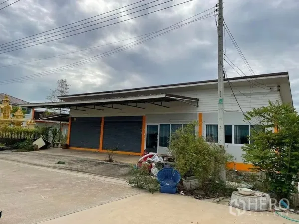Warehouse for rent or sale in Pathum Thani - Single-story shopfront with twin roller shutters and a covered loading canopy.