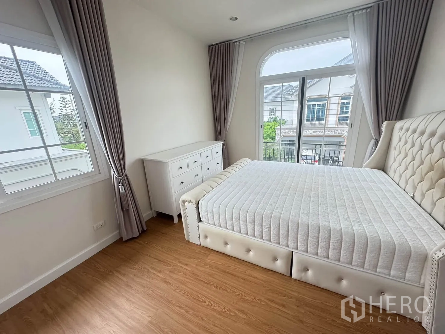 Detached House for rent or sale in Bang Phli, Samut Prakan - Bedroom with upholstered bed, dresser, wood floors, large windows and balcony access.