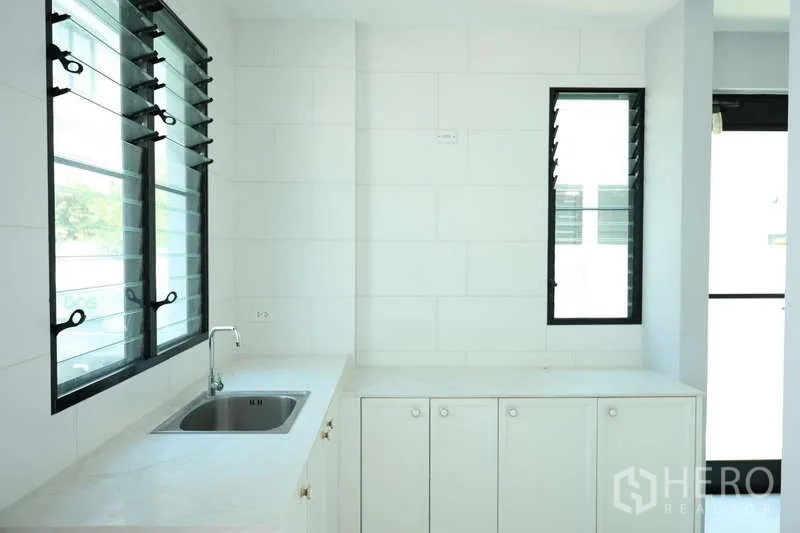 Detached House for rent or sale in Saphan Sung, Bangkok - Separate Thai kitchen with sink, white cabinetry and louvered windows.