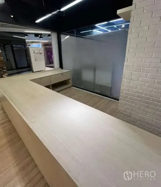 Retail Space for rent in Watthana, Bangkok - Modern retail interior with an L-shaped wood service counter, glass partition, white brick wall, and track lighting.