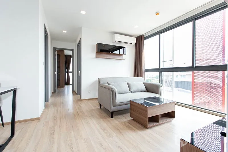 公寓 出租在Watthana, Bangkok - 采光充足的客厅，落地窗、灰色沙发与浅色木地板，Taka Haus Ekkamai。