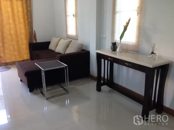 Detached House for sale in Phra Khanong, Bangkok - Cozy lounge with a brown sectional sofa and a console table beside tall windows.
