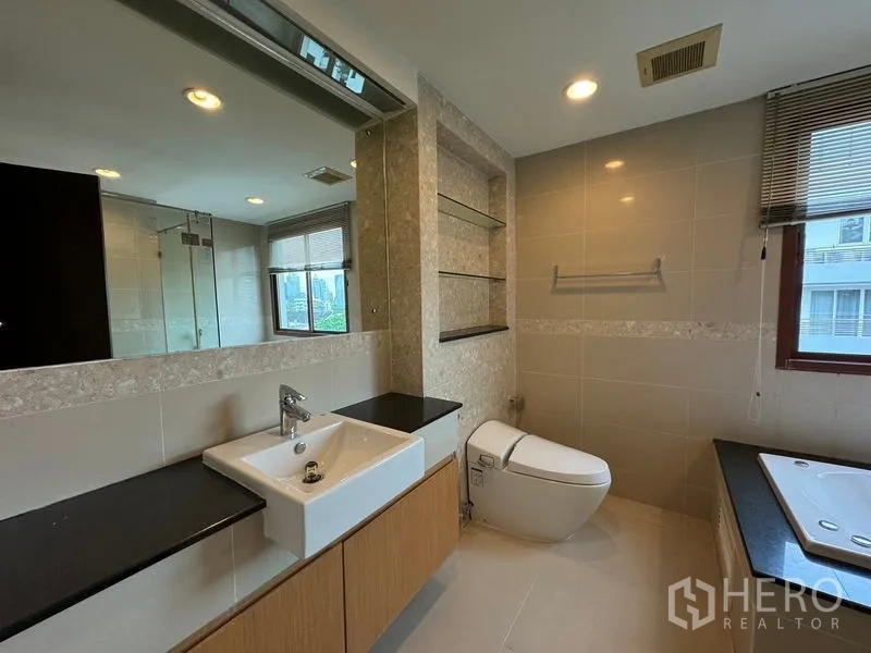 Condominium for rent in Pathum Wan, Bangkok - Bright bathroom with large mirror, smart toilet, vanity, and soaking tub.