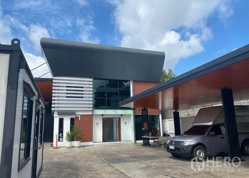 Home Office for rent or sale in Bang Khae, Bangkok - Contemporary two-storey home office in Bang Khae with wide driveway and covered parking under blue sky.