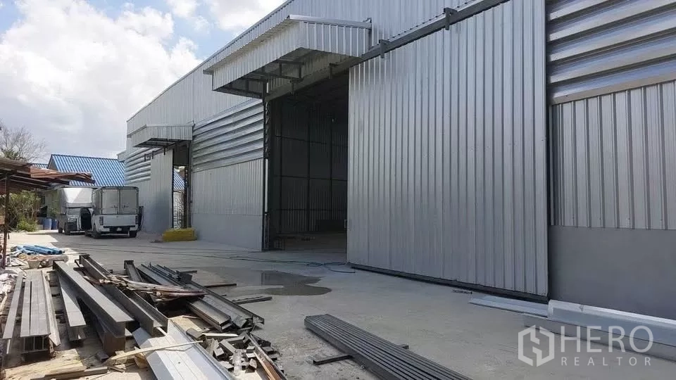 货栈 出租在Khlong Sam Wa, Bangkok - 仓库侧面装卸区，开启的库门、停放的卡车与混凝土通道。