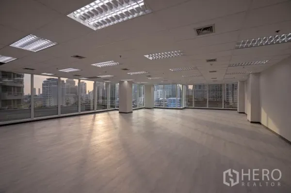 办公空间 出租在Bang Rak, Bangkok - 黄昏时的开放式办公室，环幕玻璃与自然光洒在木纹地板上。