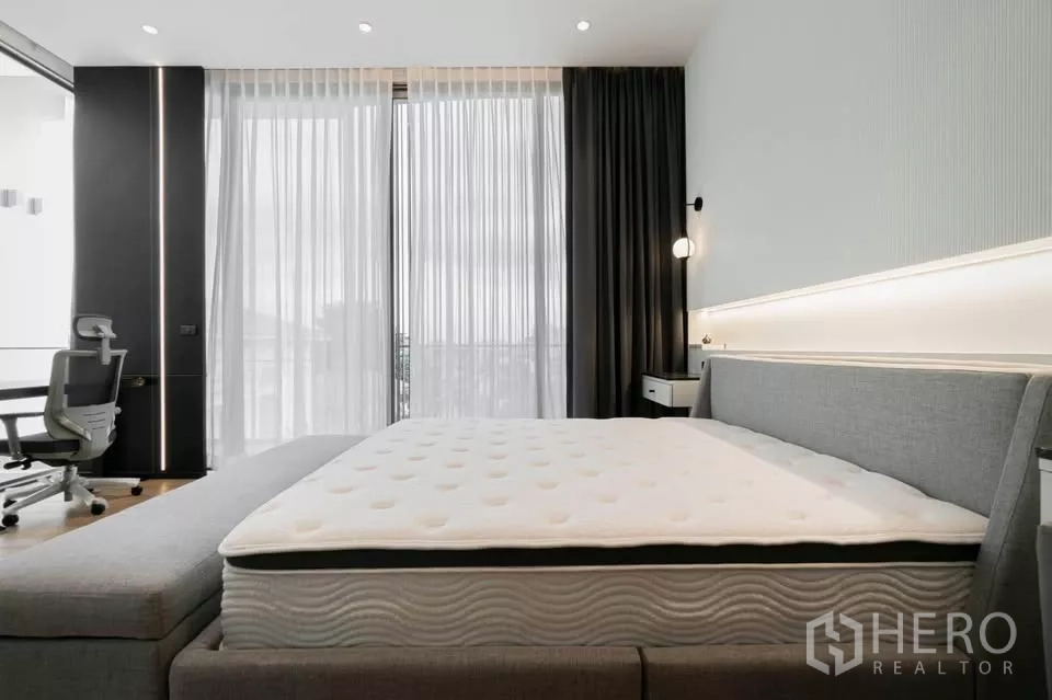 Townhouse for sale in Chatuchak, Bangkok - Master bedroom with balcony doors, desk and upholstered bed.